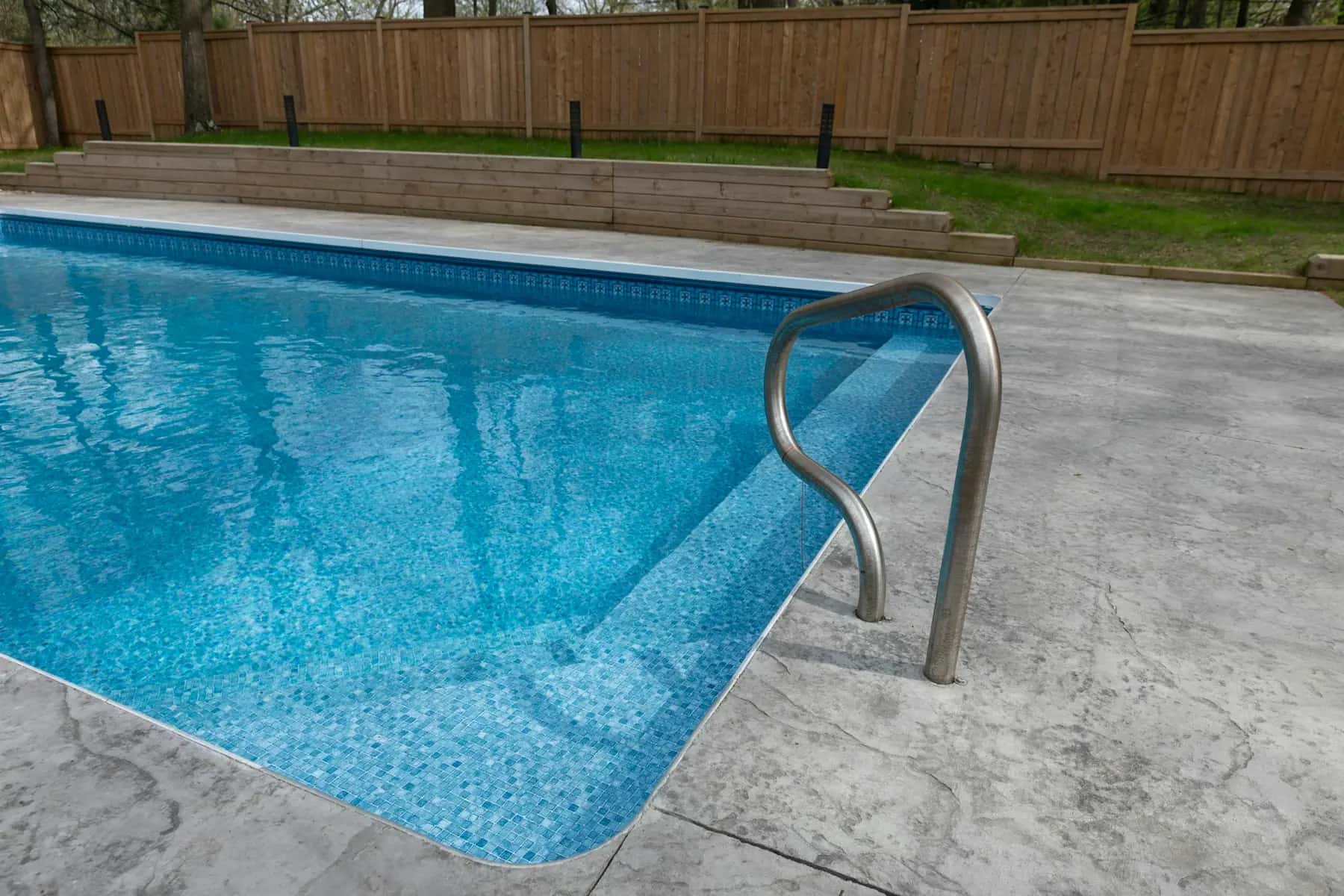 Backyard pool with a light travertine deck and wood fence